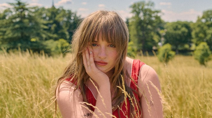 A woman in a red top with brown hair sat in a field